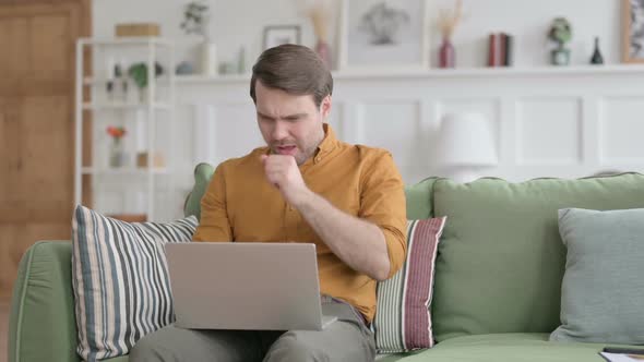 Young Man with Laptop Coughing on Sofa alt