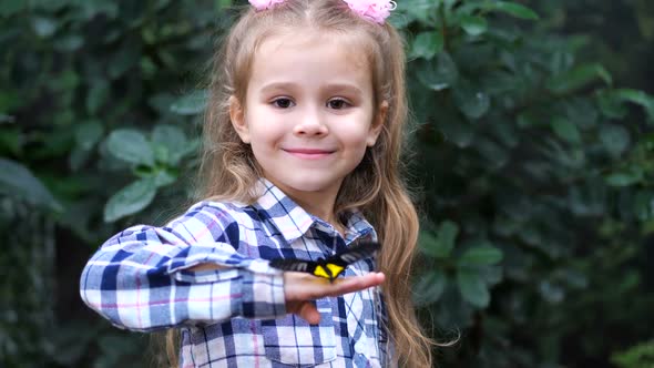 The Little Princess Holds a Butterfly on Her Hand Looks at the Frame and Smiles alt