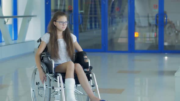 A Young Girl in a Wheelchair is Standing in the Corridor of the Hospital