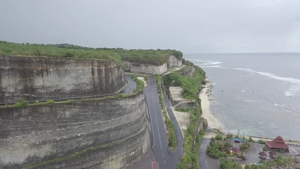 Aerial view of winding road above Melasti beach, rocky cliffs, sea waves. Cloudy. Bali Indonesia