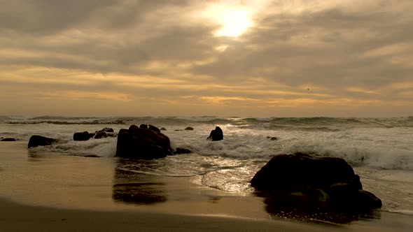 Small waves rolling over small rocks on beach during beautiful sunset and dramatic skies, golden hou alt