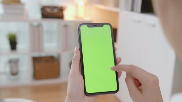 Woman holding mockup smartphone green screen with type message on the sofa at home. alt