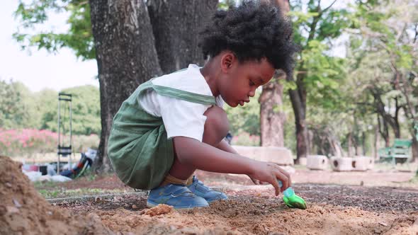 A African American child dig a hole in the sand with a toy spatula in playground in park