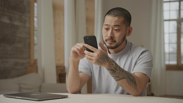A Tattoed 20s Asian Man with Like and Dislike Facial Expressions While Browsing on Smart Phone alt