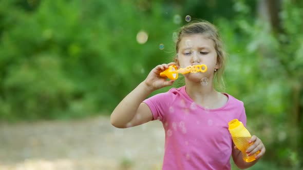 Portrait of funny lovely little girl blowing soap bubbles. Happy carefree childhood. Slow motion