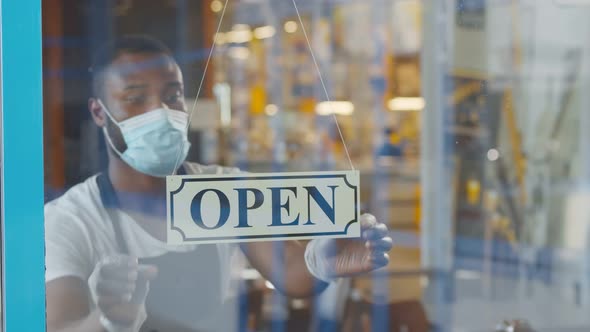 African Waiter in Mask and Gloves Putting Open Sign on Cafe Door alt