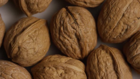 Cinematic, rotating shot of walnuts in their shells on a white surface - WALNUTS  alt