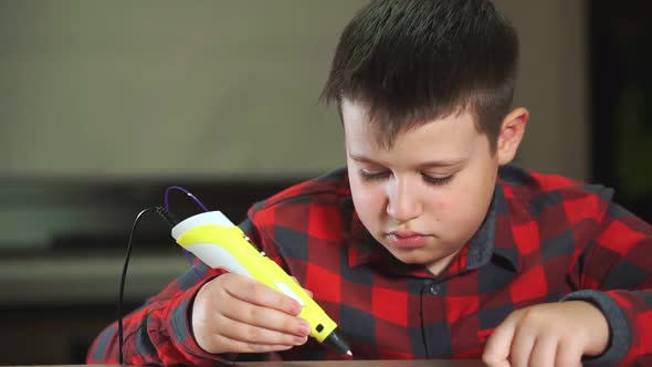 A Boy Teenager in a Plaid Shirt Draws a 3D Plastic Figure with a Pen alt