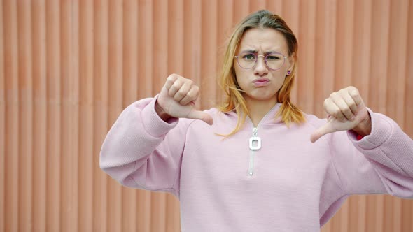 Slow Motion Portrait of Displeased Blonde Showing Thumbsdown Hand Gesture and Shaking Head Outdoors alt