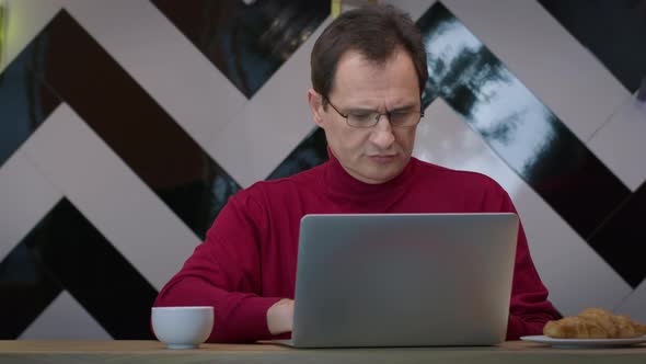 Handsome Middleaged Man Working with Laptop in Cafe