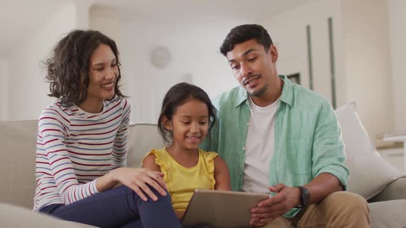 Happy hispanic parents and daughter sitting on sofa using laptop alt