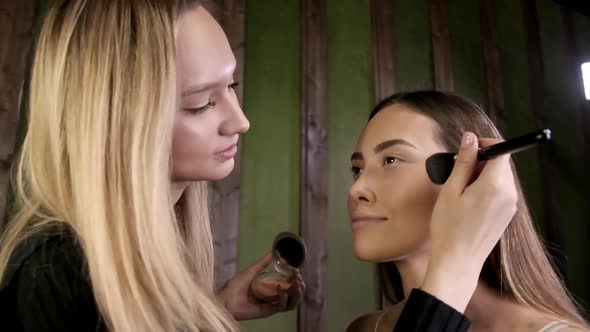 Attractive Caucasian Makeup Artist Doing Makeup for Asian Female in Beauty Salon alt