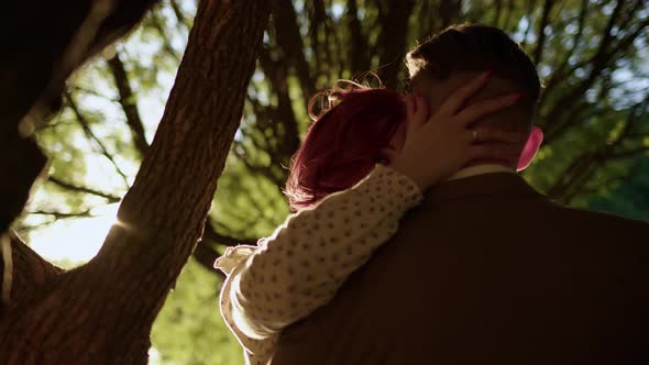 Unrecognizable Couple of Man and Woman Hugging Under Tree and Kissing Against Backdrop of Setting alt
