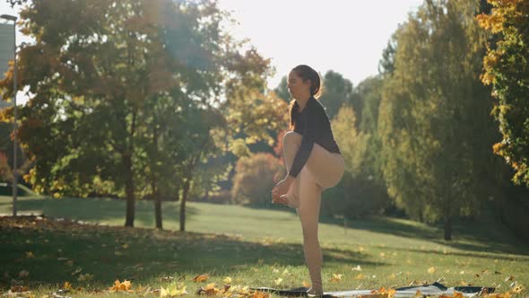Girl Practices Standing Hand to Big Toe Pose in Autumn City Park on a Yoga Mat