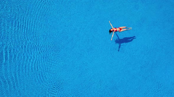View From the Top As a Woman in a Red Swimsuit Lying on Her Back in the Pool alt
