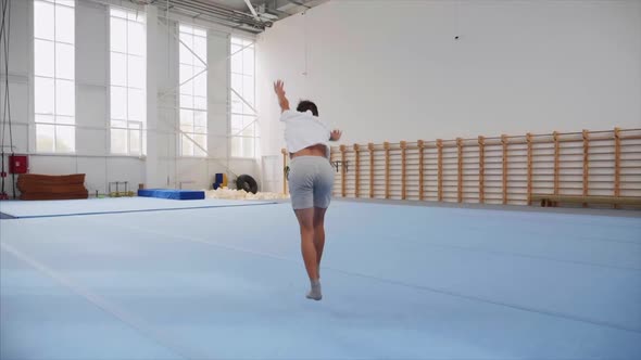 A Teenager Boy Is Doing a Cartwheel and a Triple Back Flip in Gym, Steadicam. alt