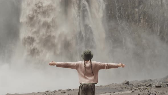 Woman traveler in hat standing with arms outstretched to the side near huge Karakaya-Su waterfall