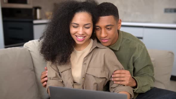 Young AfricanAmerican Couple Using Laptop While Sitting on the Sofa at Home