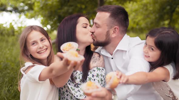 Handsome Man and Charming Woman Kissing While Their Two Cute Daughters Holding alt