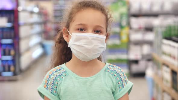 Cute Little Girl From an Epidemic of Coronaviruses or Viruses Looks at the Camera Amid Masked People alt