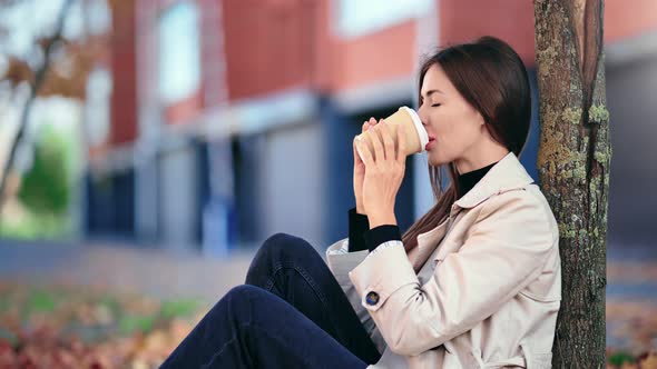 Pleasant Woman Drinking Coffee at Natural Autumn City Park alt
