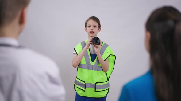 Portrait of Cute Teenage Boy in Builder Uniform Taking Photos with Camera Standing at White alt