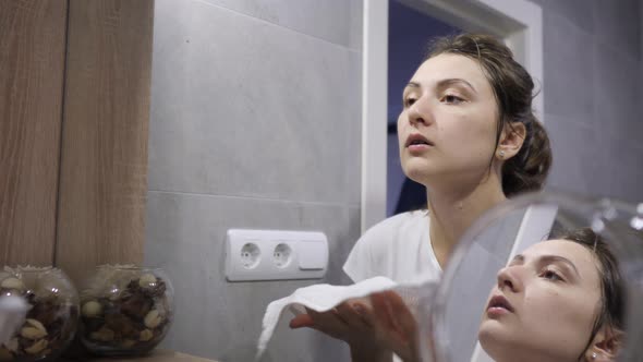 Happy Young Woman Wipes Her Face with a White Towel After Cleansing Her Face with Natural Cosmetics