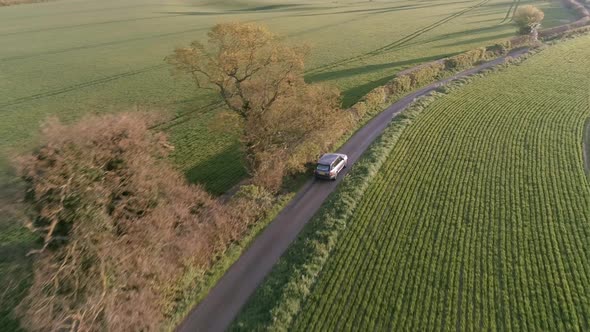 Aerial View of a Luxury SUV Driving Through a Country Lane in the Evening alt