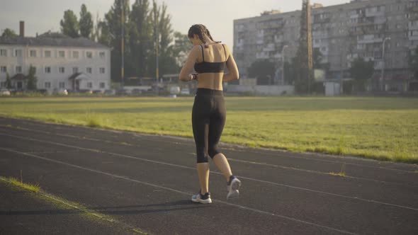 Back Angle View of Sportive Slim Woman Walking Along Athletic Field Doing Exercises. Wide Shot of alt