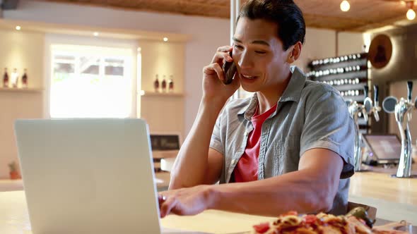 Man using laptop while talking on mobile phone in a restaurant 4k alt