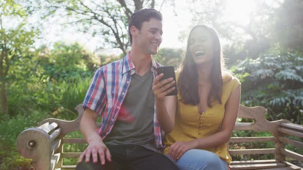 Happy caucasian couple in garden sitting on bench alt