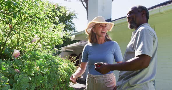Diverse senior couple in their garden looking at plants and talking in the sun alt
