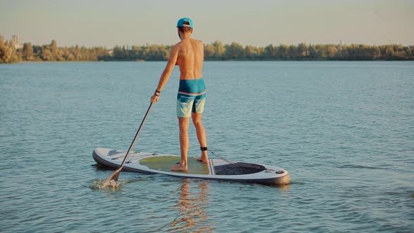 Man Floating On Sup Board At Idyllic Evening. Swimming On Stand Up Paddle Board. Surfer Water Sport alt