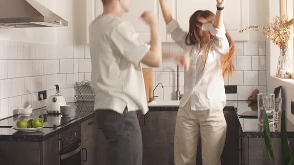 Happy Young Caucasian Married Couple Enjoy Dancing at Home in Kitchen