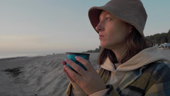 Woman drinks tea on seashore