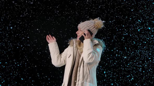 Portrait of a Beautiful Young Woman Talking on a Cell Phone While Standing Among the Falling Snow alt