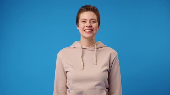 Happy Young Woman in Sweatshirt Smiling Against Blue Background