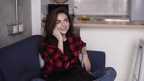 Stunningly Beautiful Girl Talking with Someone on the Phone While Holding Laptop on Her Knees alt