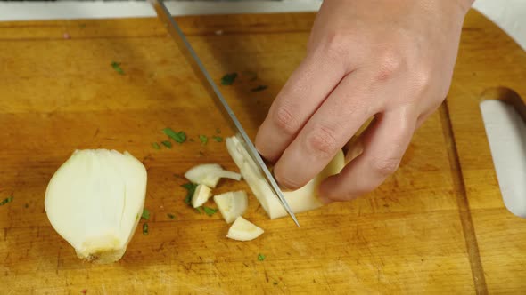 A close-up of the cook taking a peeled onion from his plate. He puts it on the kitchen board alt