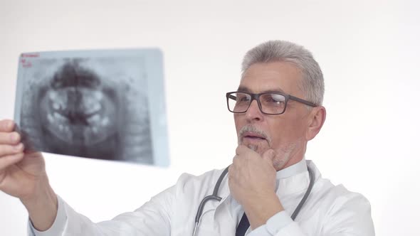 White Middleaged Doctor Man Looks Carefully at the Xray and Thoughtfully Studies Image Touching His alt
