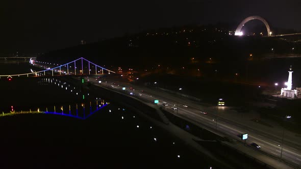 Pedestrian Bridge in Kiev. Evening Lighting. Reflection of the Bridge in the River Aerial View alt