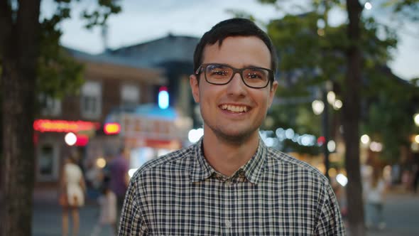 Portrait of Good-looking Student in Glasses Laughing in City Street in the Evening alt
