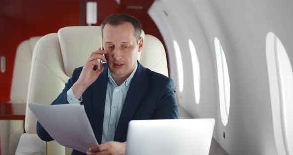 Mature Businessman Talking on Phone and Holding Document Sitting in Private Business Plane alt