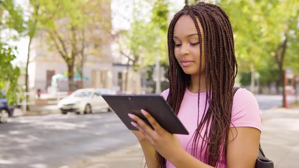 A Young Black Woman Works on a Tablet and Celebrates in the Street in an Urban Area alt