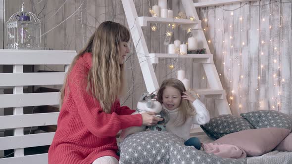 Caring Mom and Cute Blond Daughter Play with Soft Toy Deer alt