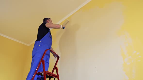 Man painting a yellow wall with a roller at work alt