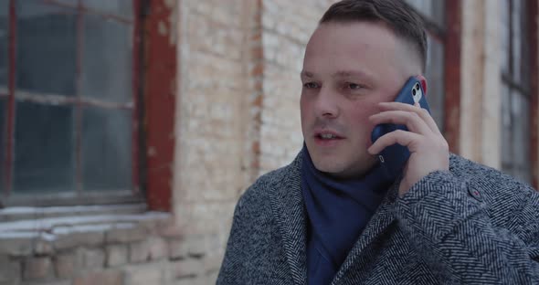 A Man Walks Down The Street And Talks On A Cell Phone With A Serious Expression