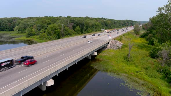 4K UHD aerial view of highway traffic; vehicles cross river on highway bridge.