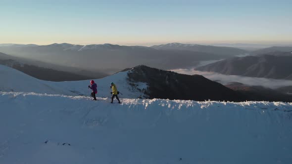 Drone Passing Couple of Hikers, Walking with Trekking Poles on Mountain Ridge in Winter