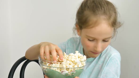 Portrait of a Funny and Excited Schoolgirl Girl on a White Background Smiling and Eating Popcorn alt